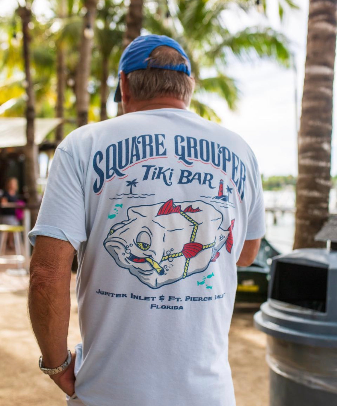 A person wearing a white Square Grouper t-shirt with a logo on the back, standing outdoors.