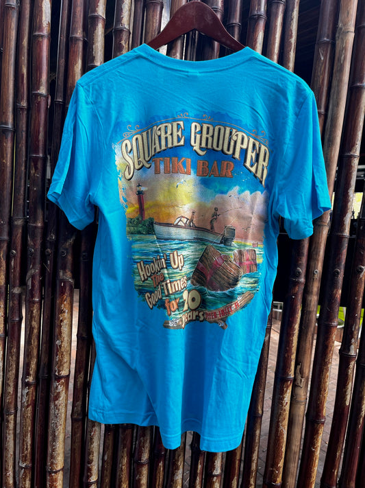 A blue t-shirt with a colorful front print depicting a beach scene and the text 'Square Grouper 20th Year' along with the logo ' Hookin Up The Good Times'.