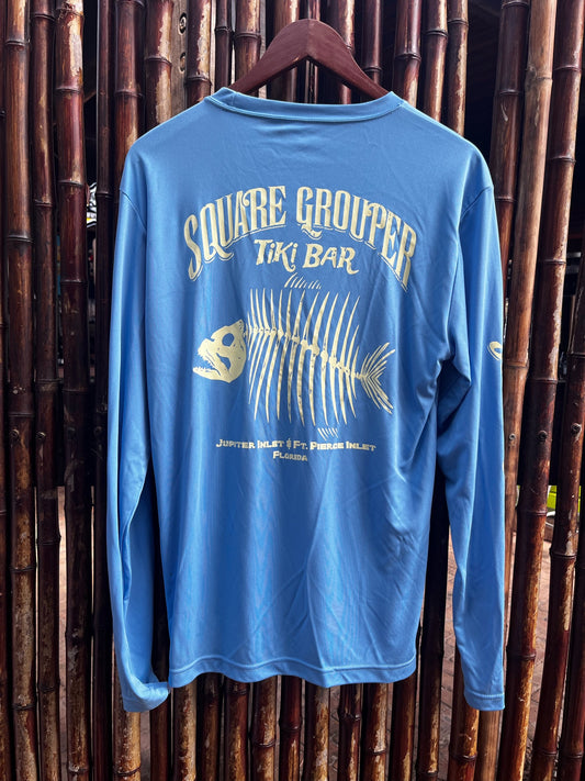 A long sleeve blue tech fabric tee with a white fish skeleton design on the back, Square Grouper logo and sleeves, displayed on a wooden hanger against a bamboo backdrop.